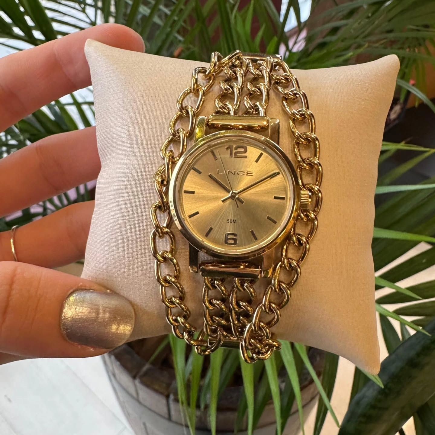 Relógio dourado com pulseira de corrente em uma almofada de exposição